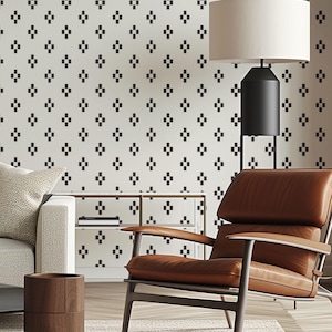 May include: A modern living room with a cream-colored sofa, brown leather armchair, and a glass-top coffee table. The wall is decorated with a repeating black diamond pattern. A black floor lamp with a white lampshade provides light. The room has a neutral color palette.
