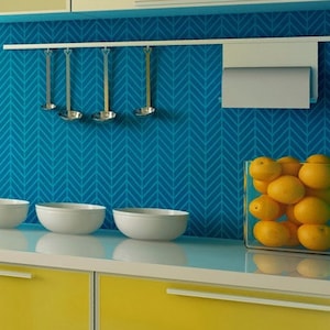 May include: A kitchen with yellow cabinets and a blue chevron patterned backsplash. There are three white bowls on the counter and a clear glass container filled with oranges. A white paper towel holder is mounted on the wall above the counter.