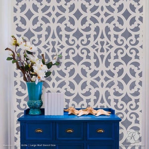 May include: A blue dresser with gold handles holds white books and starfish. A turquoise vase with white flowers sits on top. The background features a gray and white patterned wall stencil.
