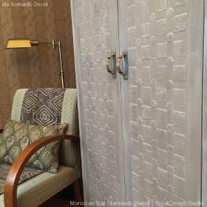 May include: A white wooden cabinet with two doors, each with a brass handle. The doors are decorated with a Moroccan star diamonds stencil pattern. The cabinet is in a room with a brown wall and a chair with a patterned cushion.