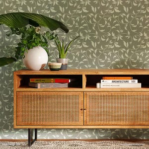 May include: A wooden cabinet with two doors and a shelf. The cabinet has a woven rattan design on the doors. The cabinet is in front of a wall with a green and white leafy vine pattern.