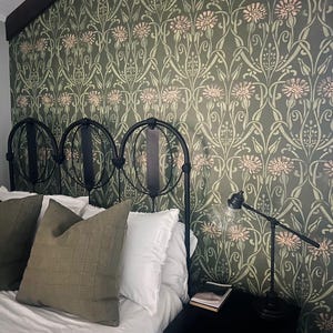 May include: A bedroom with a green and white patterned wallpaper, a black metal bed frame, white bedding, and a green pillow. A black nightstand with a book and a lamp is next to the bed.