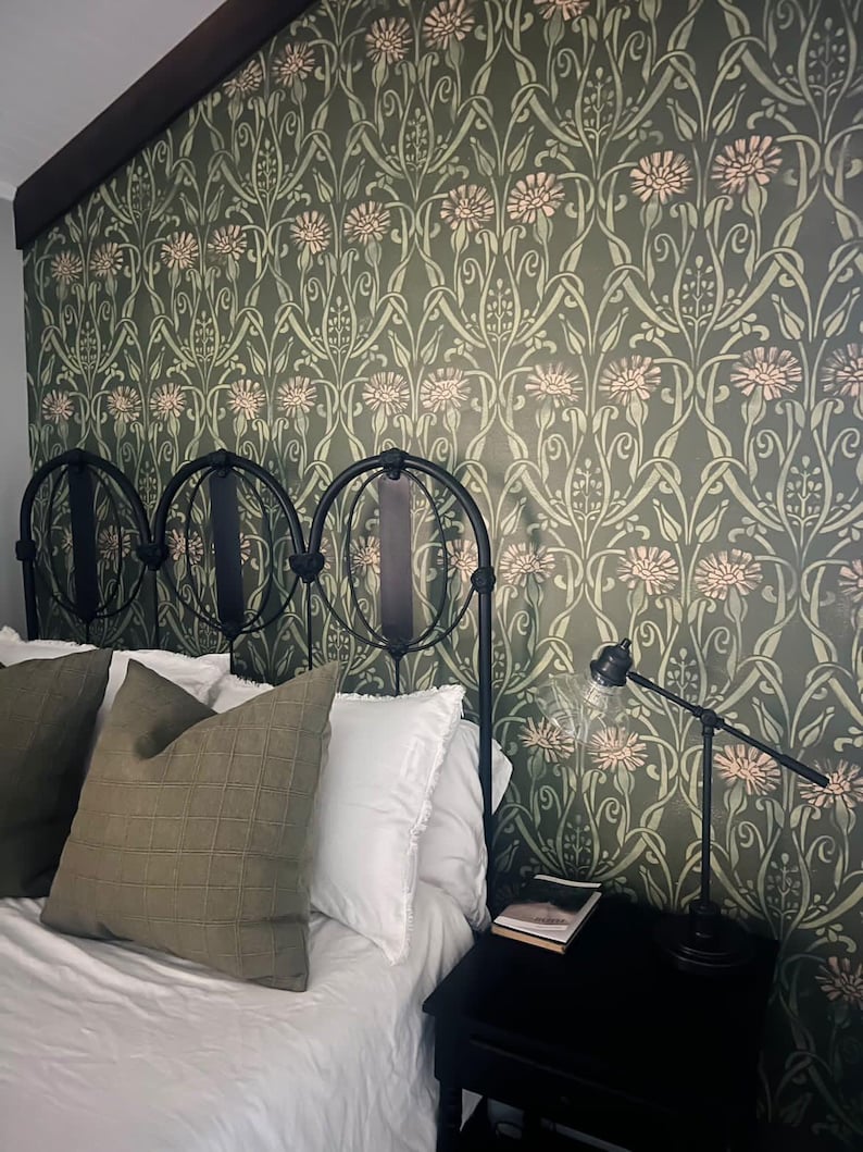 May include: A bedroom with a green and white patterned wallpaper, a black metal bed frame, white bedding, and a green pillow. A black nightstand with a book and a lamp is next to the bed.