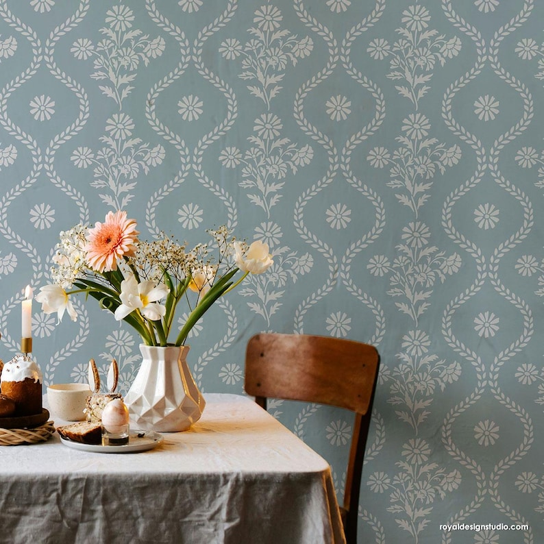 May include: A blue and white floral wallpaper stencil with a repeating pattern of daisies and leaves. The stencil is shown in a room with a table and chairs, and a vase of flowers.