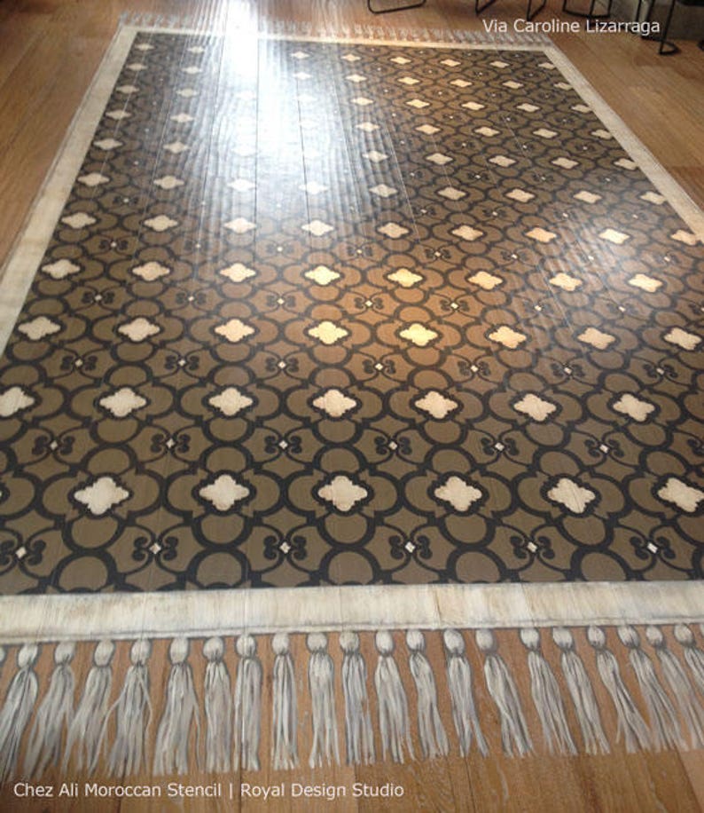 May include: A brown and white patterned floor stencil with a fringe border. The stencil is called "Chez Ali Moroccan Stencil" and is by "Royal Design Studio".