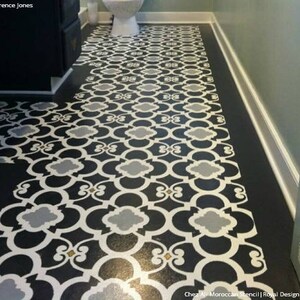 May include: A black and white patterned floor stencil with a Moroccan design. The stencil is laid out on a black floor and shows a repeating pattern of interlocking circles and squares.
