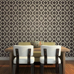 May include: Two white chairs with black straps and brown wooden legs sit at a wooden table with a brown and green bowl on top. The chairs are in front of a wall with a brown and beige geometric pattern.