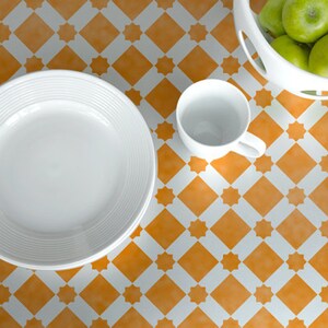 May include: A white ceramic plate and cup on a table with a yellow and white checkered pattern. The plate is stacked on top of another plate.