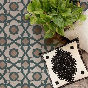 May include: A patterned floor tile with a geometric design in shades of brown and teal. A white pillow with black embroidery is on top of the tile.