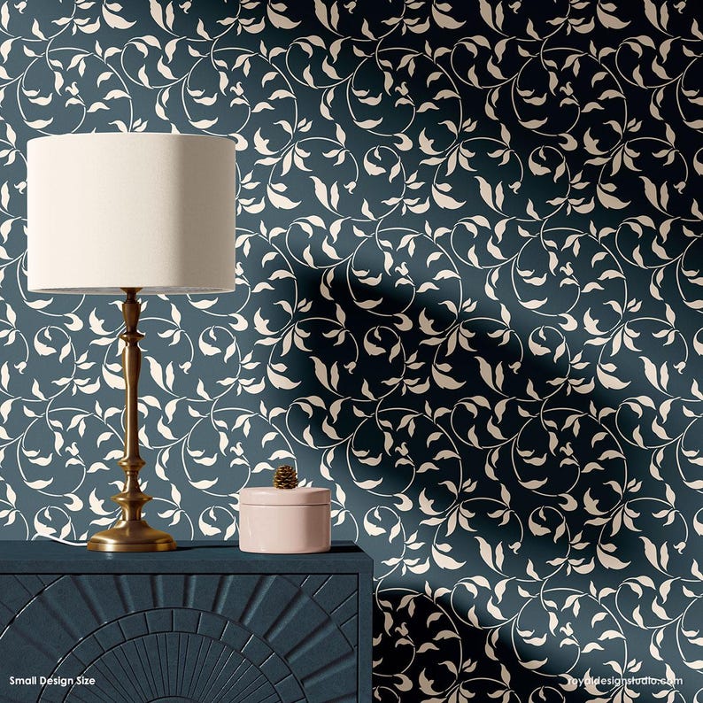 May include: A blue and white wallpaper stencil with a repeating pattern of leaves and vines. The stencil is shown on a wall with a lamp and a decorative box on a dark blue table.