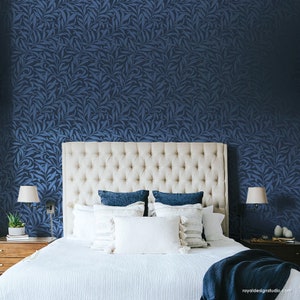 May include: A white upholstered headboard with a tufted design, a white bed with a white duvet and blue throw blanket, and a blue patterned wallpaper behind the bed.
