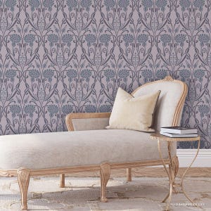 May include: A light gray chaise lounge with a pillow and a small gold side table with books on top. The chaise lounge is in front of a wall with a repeating pattern of dark gray floral designs on a light gray background.