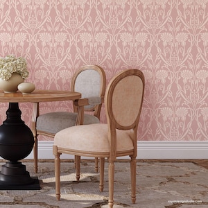 May include: Two wooden chairs with light pink upholstery sit at a wooden table in front of a pink wall with a white floral pattern.