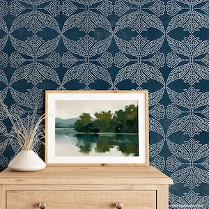 May include: A wooden dresser with two drawers and a framed landscape painting of a lake and trees. The dresser is in front of a wall with a blue and white geometric pattern.