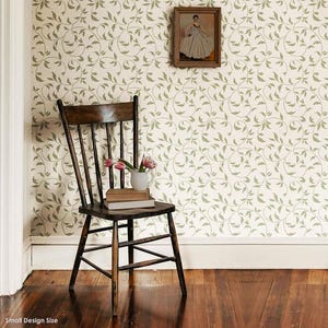 May include: A wooden chair with a light brown finish sits in front of a wall with a white background and a green vine pattern. The chair has a high back and a curved seat. There are a few books and a vase with pink flowers on the seat of the chair.