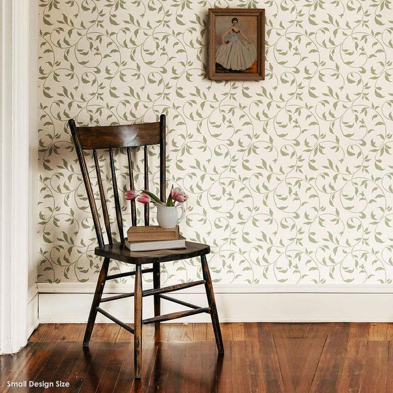 May include: A wooden chair with a light brown finish sits in front of a wall with a white background and a green vine pattern. The chair has a high back and a curved seat. There are a few books and a vase with pink flowers on the seat of the chair.
