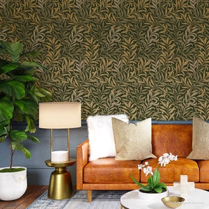 May include: A living room interior design featuring a brown leather sofa with white and beige throw pillows, a gold table lamp with a white shade, a gold side table, a potted plant with white flowers, and a gold coffee table. The wall is covered in a green and gold wallpaper with a leaf pattern.