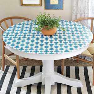 May include: White round table with a blue and white geometric pattern painted on the top. The table has a pedestal base and is sitting on a black and white striped rug.