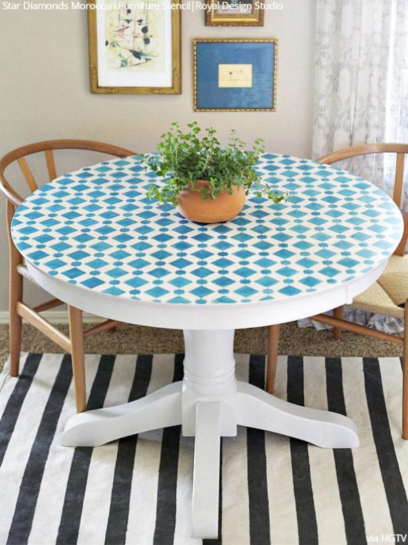May include: White round table with a blue and white geometric pattern painted on the top. The table has a pedestal base and is sitting on a black and white striped rug.