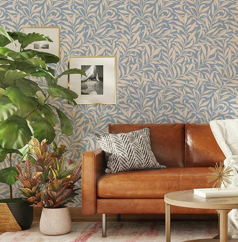 May include: A brown leather sofa with a patterned throw pillow and a small wooden table in front of it. The sofa is in front of a wall with a blue and white floral wallpaper.
