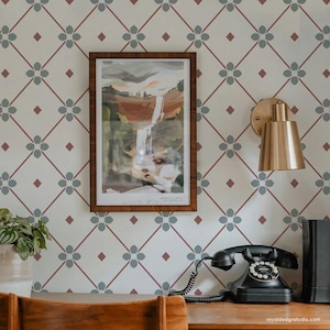 May include: A white wall with a repeating pattern of blue flowers and red diamonds. A framed watercolor painting of a waterfall hangs on the wall. A gold wall sconce is mounted on the wall to the right of the painting. A black rotary phone sits on a wooden desk in front of the wall.