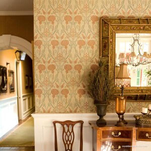 May include: A beige wall with a repeating floral pattern stencil in shades of green and orange. The stencil is on a wall in a hallway with a wooden dresser and a mirror with a gold frame.