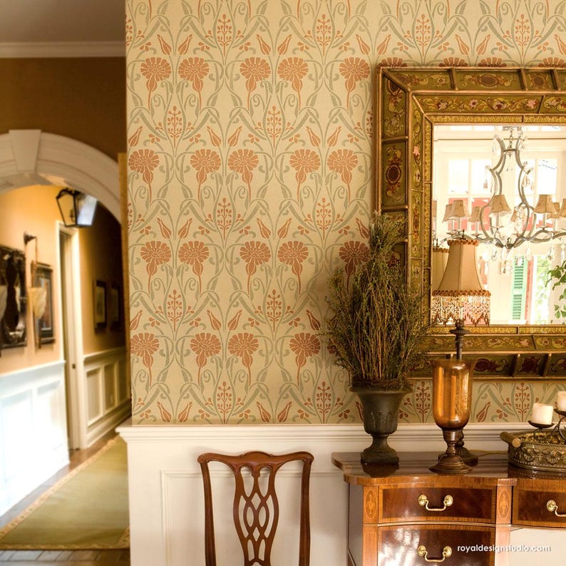 May include: A beige wall with a repeating floral pattern stencil in shades of green and orange. The stencil is on a wall in a hallway with a wooden dresser and a mirror with a gold frame.