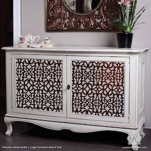 May include: White painted wooden cabinet with two doors. The doors have a brown stencil design of a repeating geometric pattern. The cabinet has a curved bottom and sits on four legs.