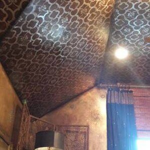 May include: A close-up of a ceiling with a decorative stencil pattern in a brown and silver color scheme. The stencil pattern is a repeating geometric design. The ceiling is angled and the room is decorated in a similar style.
