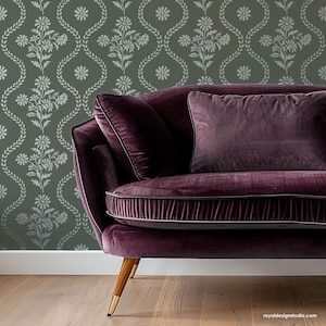 May include: A purple velvet sofa with a floral patterned wallpaper behind it. The sofa has a tufted back and a gold metal base.