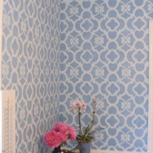 May include: A blue wall with a white stencil pattern. The wall is decorated with pink flowers in a pot. The text "Chez Ali Stencil | Royal Design Studio" is visible at the bottom of the image.