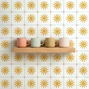 May include: Four pastel-colored ceramic mugs on a wooden shelf against a patterned background. The background features a repeating pattern of yellow suns, light blue dots, and pink crosses on a white surface. The mugs are in shades of pink, light green, yellow, and light pink.