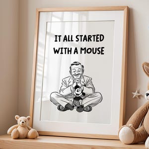 Puede incluir: Un estampado en blanco y negro enmarcado con el texto "IT ALL STARTED WITH A MOUSE" y una ilustración de un hombre sosteniendo un muñeco de Mickey Mouse. El estampado está en un marco de madera clara y se encuentra en un estante de madera con peluches.