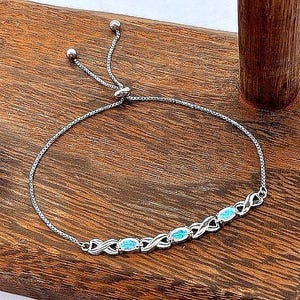 May include: A silver-toned adjustable bolo bracelet featuring a delicate chain and a central decorative section. This section consists of three oval-shaped, iridescent blue stones set within a repeating infinity-style metal link pattern.