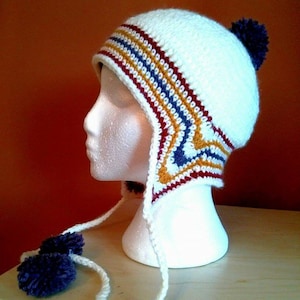 May include: White crocheted hat with colorful stripes and ear flaps. The hat has a purple pom-pom on top and two purple pom-poms on the ear flaps.