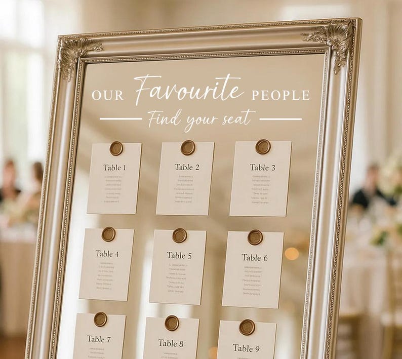 May include: A framed seating chart with the text "OUR Favourite PEOPLE Find your seat." Nine cards are displayed, each labeled "Table" followed by a number, and affixed with a circular seal. The frame is ornate and silver.