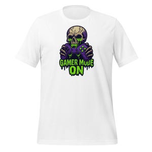 Könnte beinhalten: Weißes T-Shirt mit einer Grafik eines Schädels, der einen lila Videospiel-Controller hält. Der Schädel hat grüne tropfende Akzente, und der Text "GAMER MODE ON" steht darunter in Grün.
