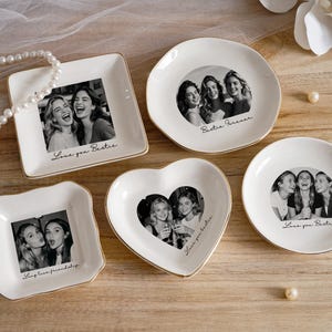 May include: A set of white ceramic trinket dishes in different shapes, including square, round, and heart-shaped. Each dish has a black and white photograph of friends and a gold rim. Text includes "Love you Bestie" and "Bestie Forever".