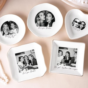 Puede incluir: Colección de cuencos de cerámica blanca para baratijas en varias formas, incluyendo redondos, de corazón y cuadrados. Cada cuenco presenta una fotografía en blanco y negro de amigos y ribete dorado. Texto: "Love you Bestie."