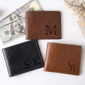 Puede incluir: Se muestran tres carteras de cuero en marrón y negro, cada una con iniciales o un nombre personalizados. Una cartera marrón tiene grabado "MARTIN". La cartera negra tiene "S|K" y la otra cartera marrón tiene "C|H". Se ven billetes.