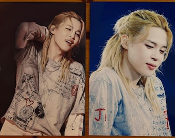 May include: Two rectangular photographic prints featuring a person with blonde hair styled in a half-up ponytail. The person wears a light-colored t-shirt with black text, graphic illustrations, and red accents. The prints show the person in different poses.