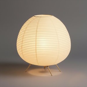 Può includere: Lampada a lanterna sferica in carta bianco sporco, con una calda illuminazione. La lampada ha una trama a coste e poggia su tre sottili gambe color oro. Design minimalista e moderno, adatta all'arredamento della casa.