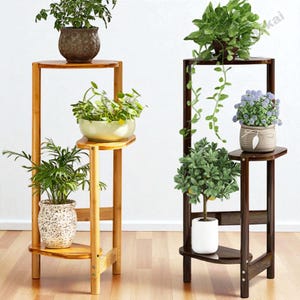 Peut inclure: Deux présentoirs à plantes en bois, l'un brun clair et l'autre brun foncé, chacun avec trois niveaux. Les présentoirs contiennent diverses plantes en pot avec des feuilles vertes et des fleurs. Les présentoirs sont en bois et ont un design simple et moderne.