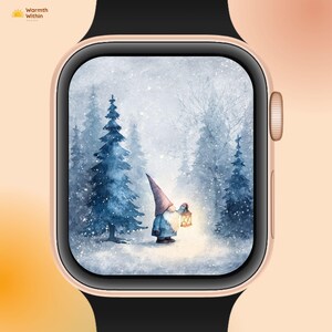 Puede incluir: Un smartwatch con caja dorada y correa negra muestra una escena invernal. La pantalla muestra una pintura de acuarela de un gnomo con una linterna en un bosque nevado. El texto "Warmth Within" está en la esquina superior izquierda.