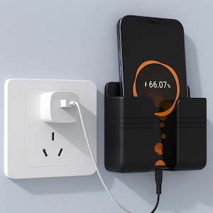 Puede incluir: Soporte de teléfono negro montado en la pared con un teléfono inteligente cargando. El teléfono muestra un progreso de carga del 66,07%. Un enchufe y un cargador blancos son visibles a la izquierda. El soporte está montado en una pared azul claro.