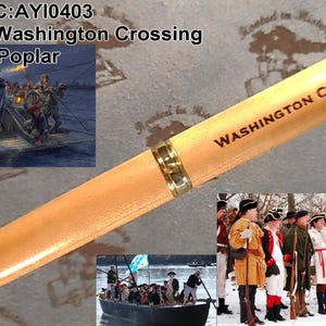 May include: A light brown pen with gold accents and the words "WASHINGTON CROSSING" printed on the barrel. The pen features images of George Washington and historical scenes. The pen is made of poplar wood.