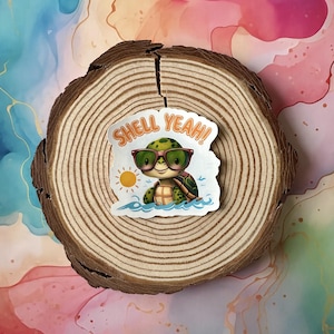 May include: A sticker depicting a cartoon turtle wearing sunglasses and floating in water. The sticker has the text "SHELL YEAH!" and a small sun graphic. The sticker is placed on a wooden slice with a colourful background.