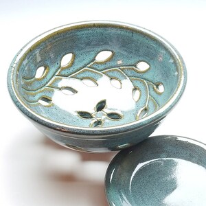 May include: A teal blue ceramic bowl with a leafy design and cut-out holes. The bowl is paired with a matching teal blue saucer.