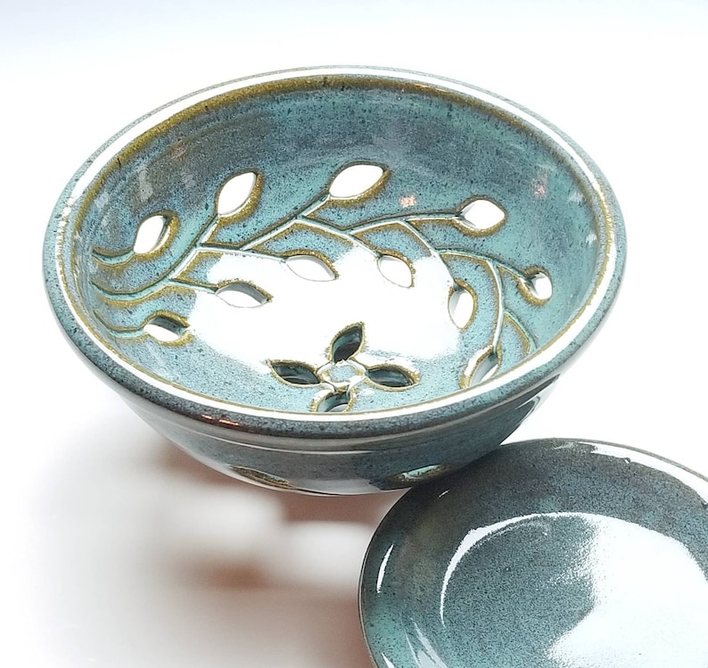 May include: A teal blue ceramic bowl with a leafy design and cut-out holes. The bowl is paired with a matching teal blue saucer.