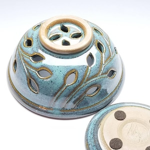 May include: A teal blue ceramic incense burner with a leaf design and a small hole in the top. The burner has a matching base with four small feet.